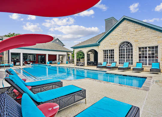A large swimming pool with lounge chairs and a building in the background.