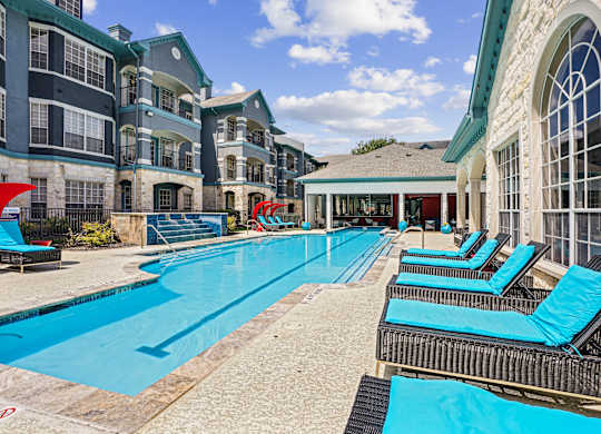 A large swimming pool with lounge chairs and a building in the background.