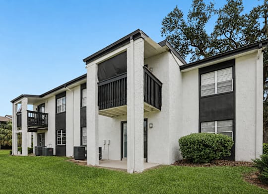 A white and black two-story apartment building with a balcony on the second floor.