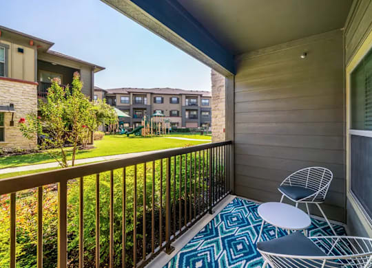 A balcony with a table and chairs overlooking a grassy area.
