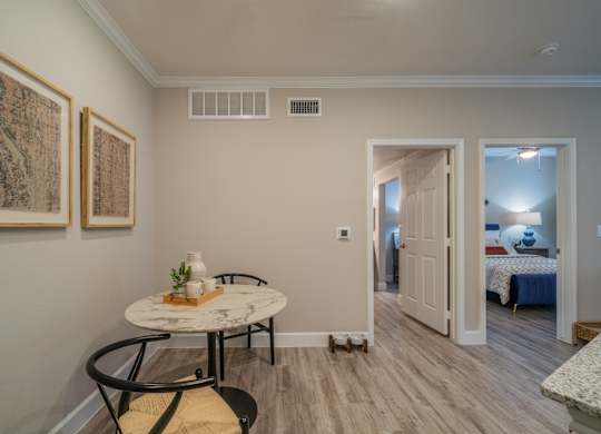 a small table with two chairs in the corner of a room with a bedroom in the background