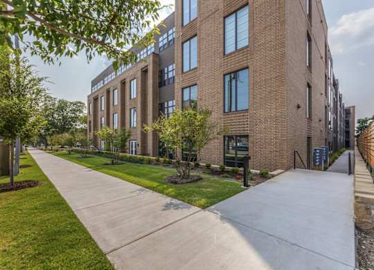 A long concrete walkway leads to a brick building with a green lawn on the side.