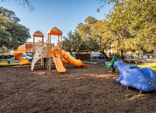 A playground with a yellow and orange slide and a blue slide.