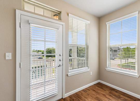 A room with a white door and two windows with white blinds.