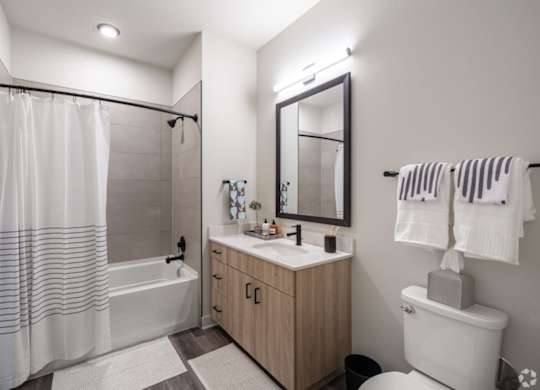 A modern bathroom with a white toilet, a white sink, a white shower curtain, and a wooden cabinet.
