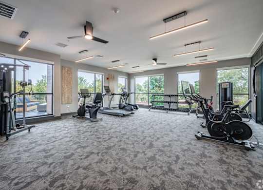 A spacious gym with a variety of exercise equipment and large windows.