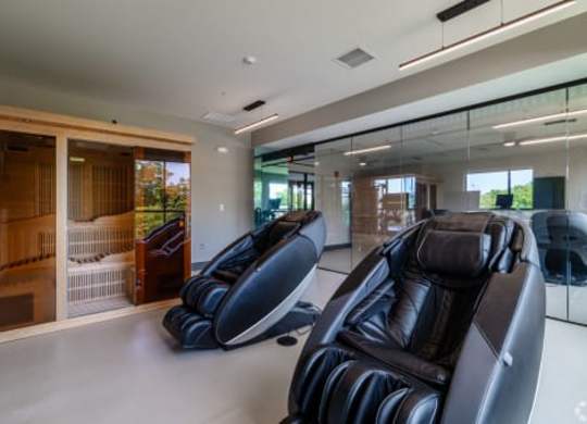 Two black leather recliner chairs are in a spacious room with a glass wall and a wooden door.