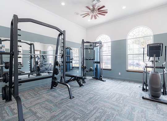 A gym with a variety of equipment including a squat rack, a leg press machine, and a treadmill.