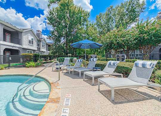 A pool with a blue umbrella and chairs.