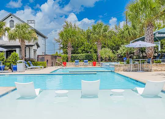 A pool with white chairs and a house in the background.