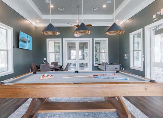 A pool table is in the middle of a room with a wooden floor and a ceiling fan.