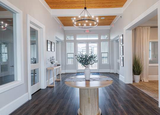 A large, round wooden table is at the center of a spacious room with a chandelier hanging from the ceiling.