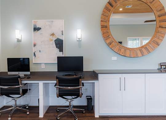 Two computers are on a desk with a mirror and two lights above.