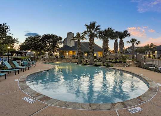 A large outdoor swimming pool surrounded by palm trees and lounge chairs.