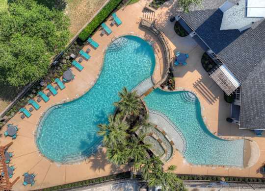An aerial view of a swimming pool surrounded by palm trees and lounge chairs.