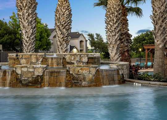 A pool with a waterfall and palm trees in the background.