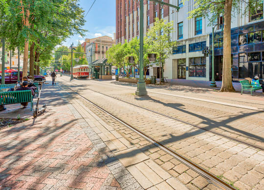 a city street with streetcar tracks and people sitting on benches