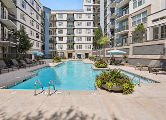 A swimming pool surrounded by lounge chairs and planters in a courtyard.