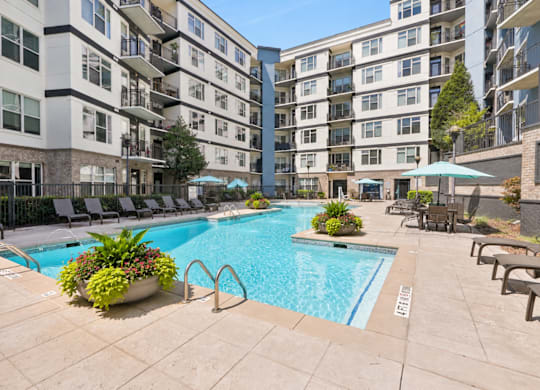 A large swimming pool surrounded by lounge chairs and umbrellas in a courtyard.