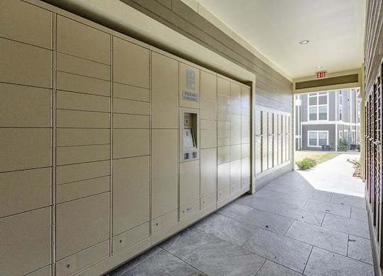 A long hallway with a wall of lockers and a red exit sign at the end.