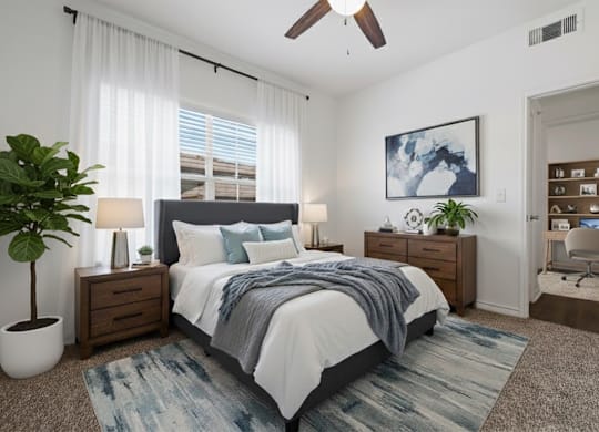 A bedroom with a bed, a plant, a ceiling fan, and a painting on the wall.