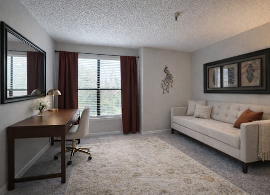 A well-lit room with a desk, chair, and couch.