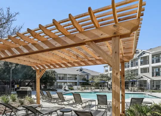 A wooden pergola over a poolside lounge area.
