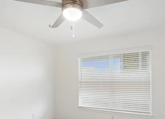 A room with a ceiling fan and a window with blinds.