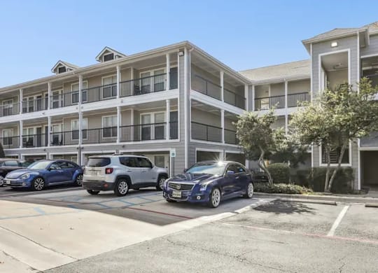 A parking lot in front of a multi-story apartment building with cars parked.