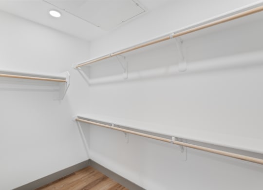 a walk in closet with white walls and a wood floor