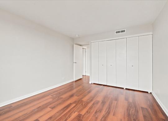 A room with wooden floors and white walls with a row of white cupboards.