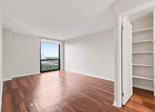 A bedroom with wooden floors and floor to ceiling windows and spacious closet.