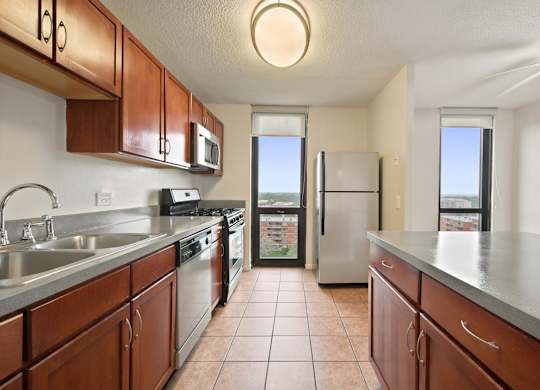A tiled kitchen with an island, brown cabinets and stainless stain appliances.