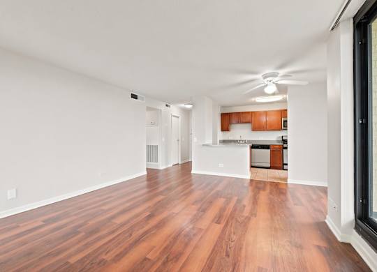 A living room with wooden floors and ceiling fan with the kitchen in the background.