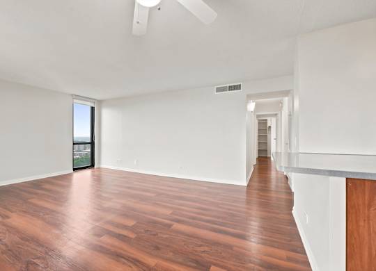 A living room with wooden floors, ceiling fan, and bar island of the kitchen.