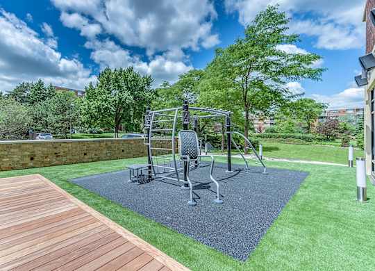 A park with a wooden walkway, a black exercise machine, and a green lawn.