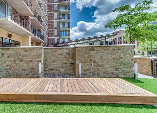 A wooden deck with a stone wall and green grass in the foreground.