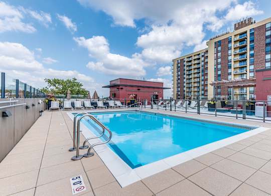A pool surrounded by a red building and a tall building in the background.