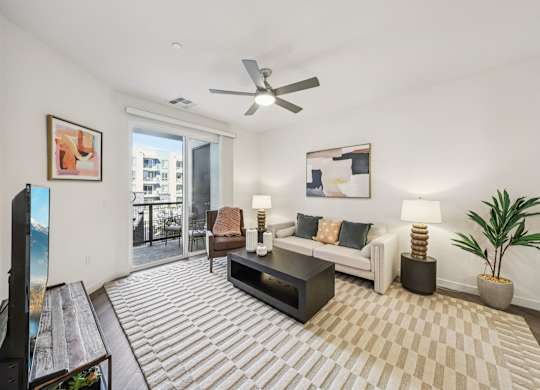 A living room with a white couch, a coffee table, and a ceiling fan.at Fora Apartments, Nevada