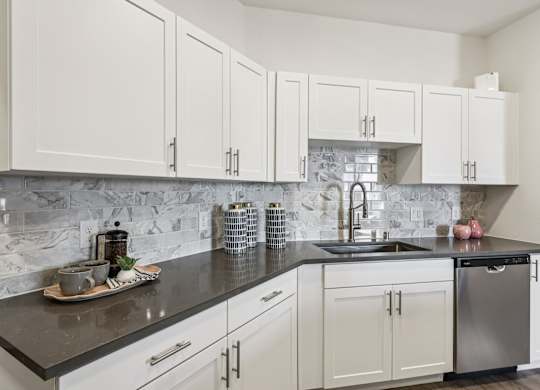 A kitchen with white cabinets and a marble backsplash.at Fora Apartments, Las Vegas, NV 89183