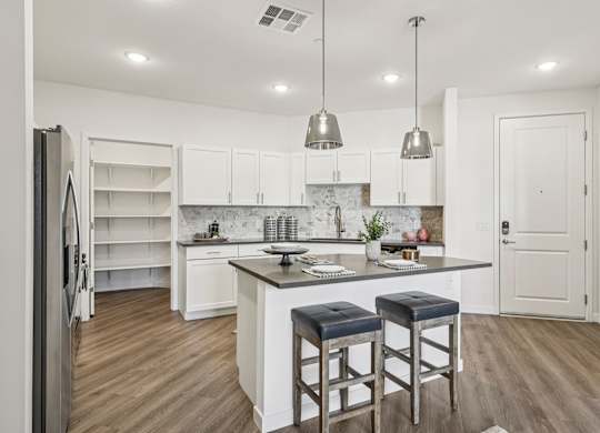 A kitchen with white cabinets and a marble island.at Fora Apartments, Nevada