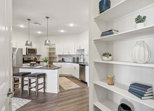 A kitchen with white cabinets and a white island with a bar stool.at Fora Apartments, Las Vegas Nevada