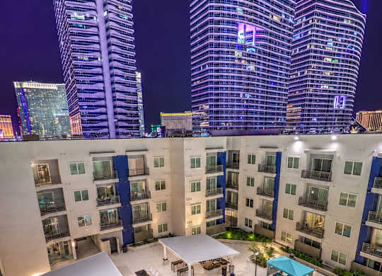 A swimming pool with loungers and umbrellas is surrounded by apartment buildings.