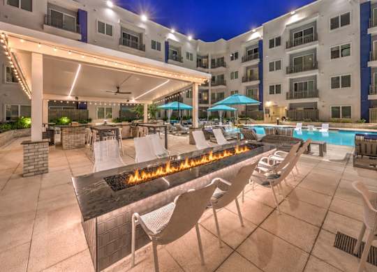 A patio with a fire pit and chairs is illuminated at night.