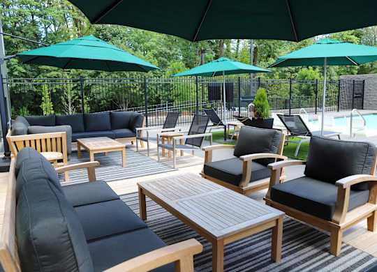 A patio with black cushioned chairs and tables under green umbrellas.