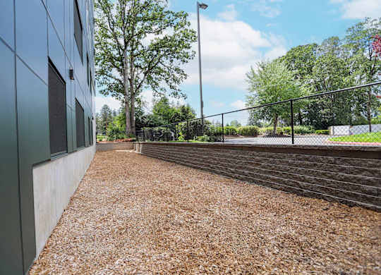 A gravel pathway leads to a fenced area with trees in the background.