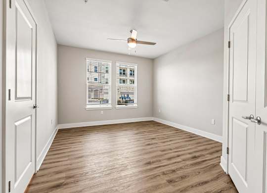 A room with a ceiling fan and two windows with pictures on the wall.