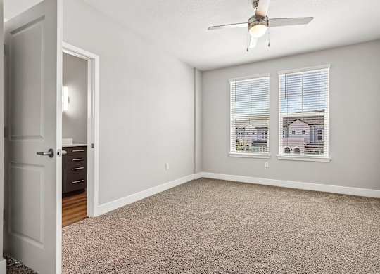 A room with a carpeted floor, a ceiling fan, and a window with blinds.