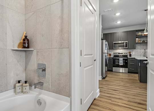 A bathroom with a tub and a kitchen in the background.
