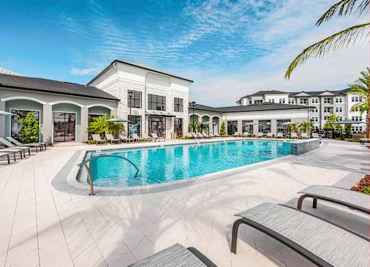 A large swimming pool is surrounded by lounge chairs in front of a building.
